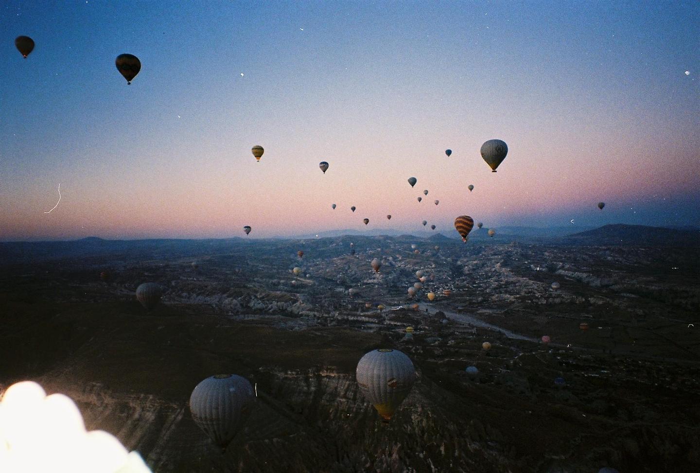 Hot air balloons float over a valley at dusk.