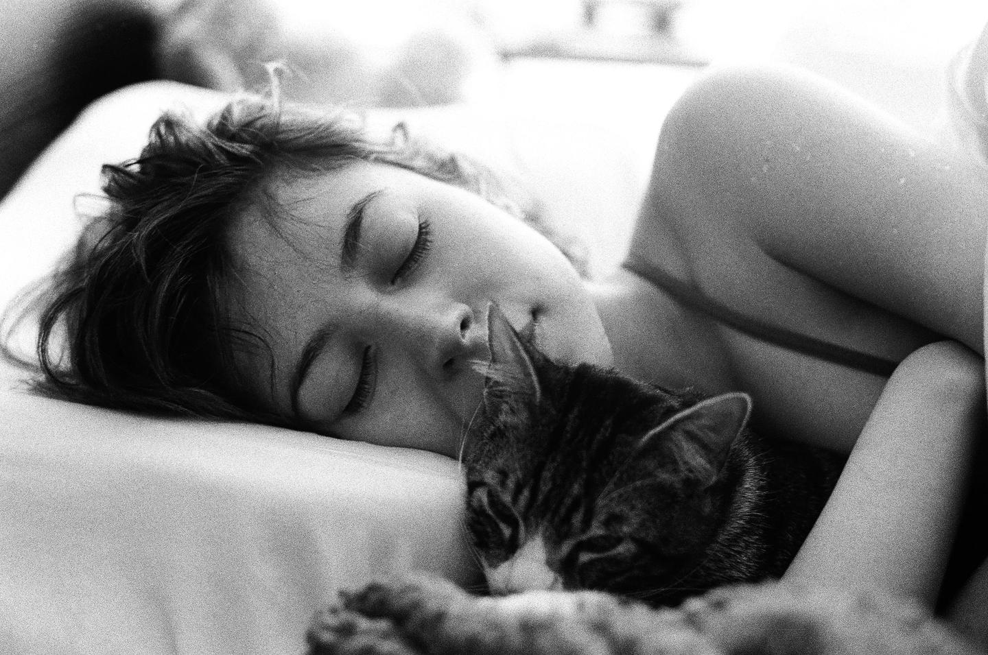 A woman and a cat are sleeping together in a bed.