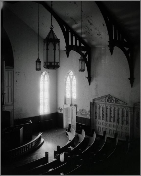 An abandoned church interior is seen from an elevated perspective, featuring arched windows, hanging lanterns, and rows of pews.