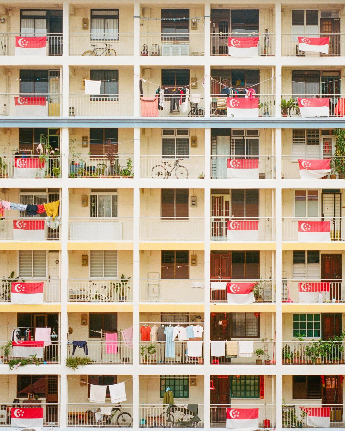 A grid of balconies on a housing complex is adorned with many Singaporean flags and laundry.