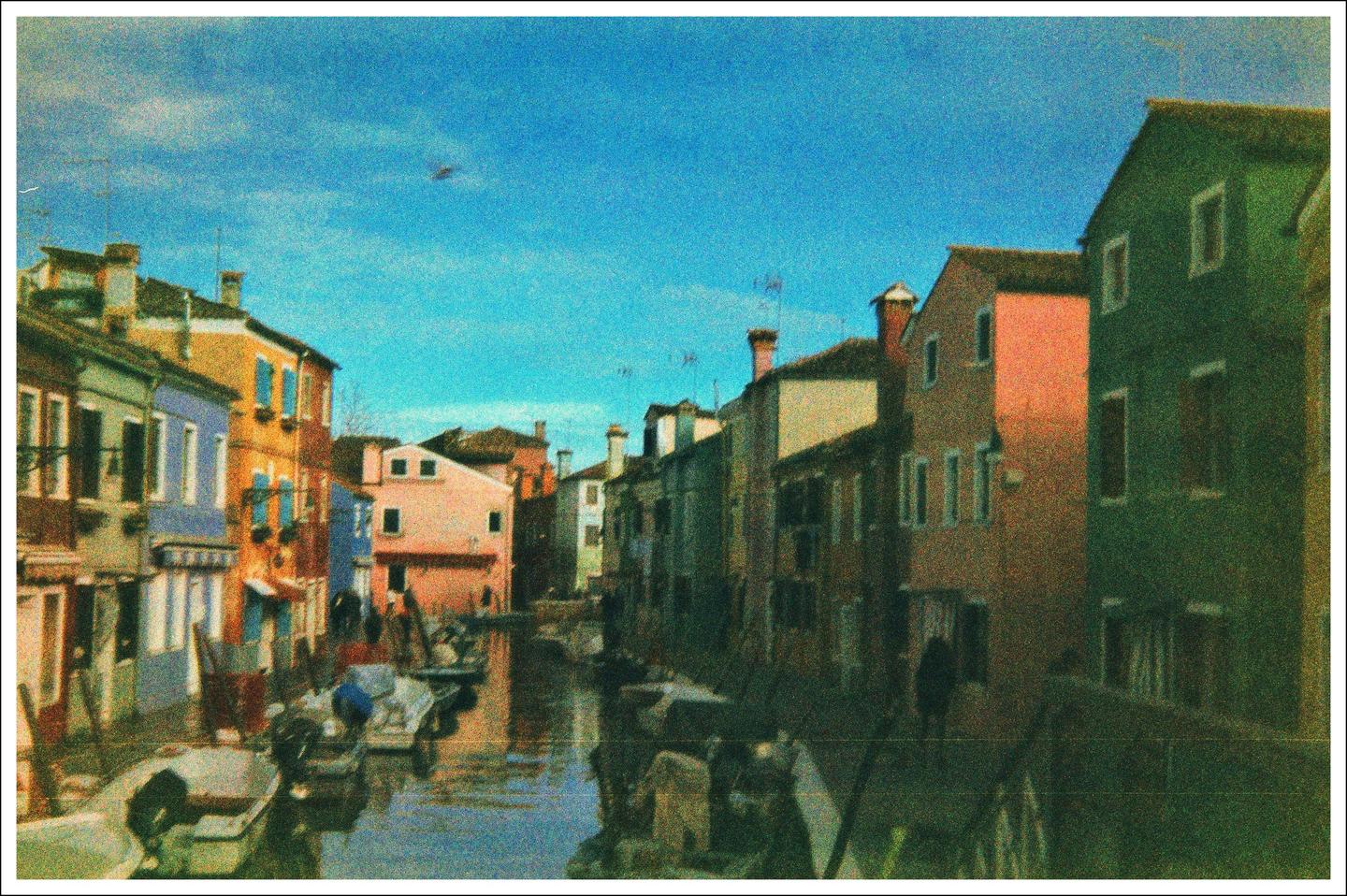 A canal with boats is lined by colorful buildings under a bright blue sky.