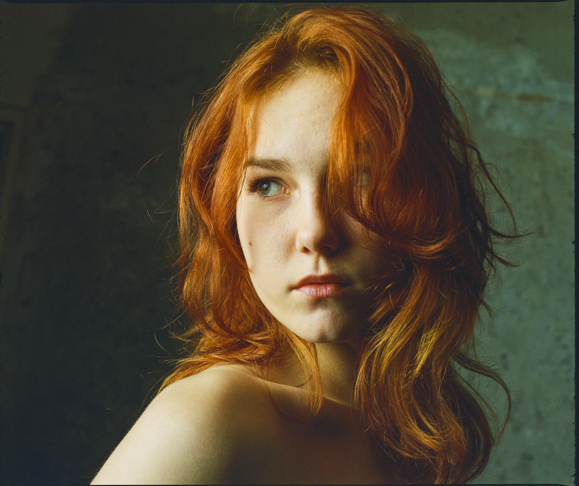 A woman with long red hair looks over her shoulder.