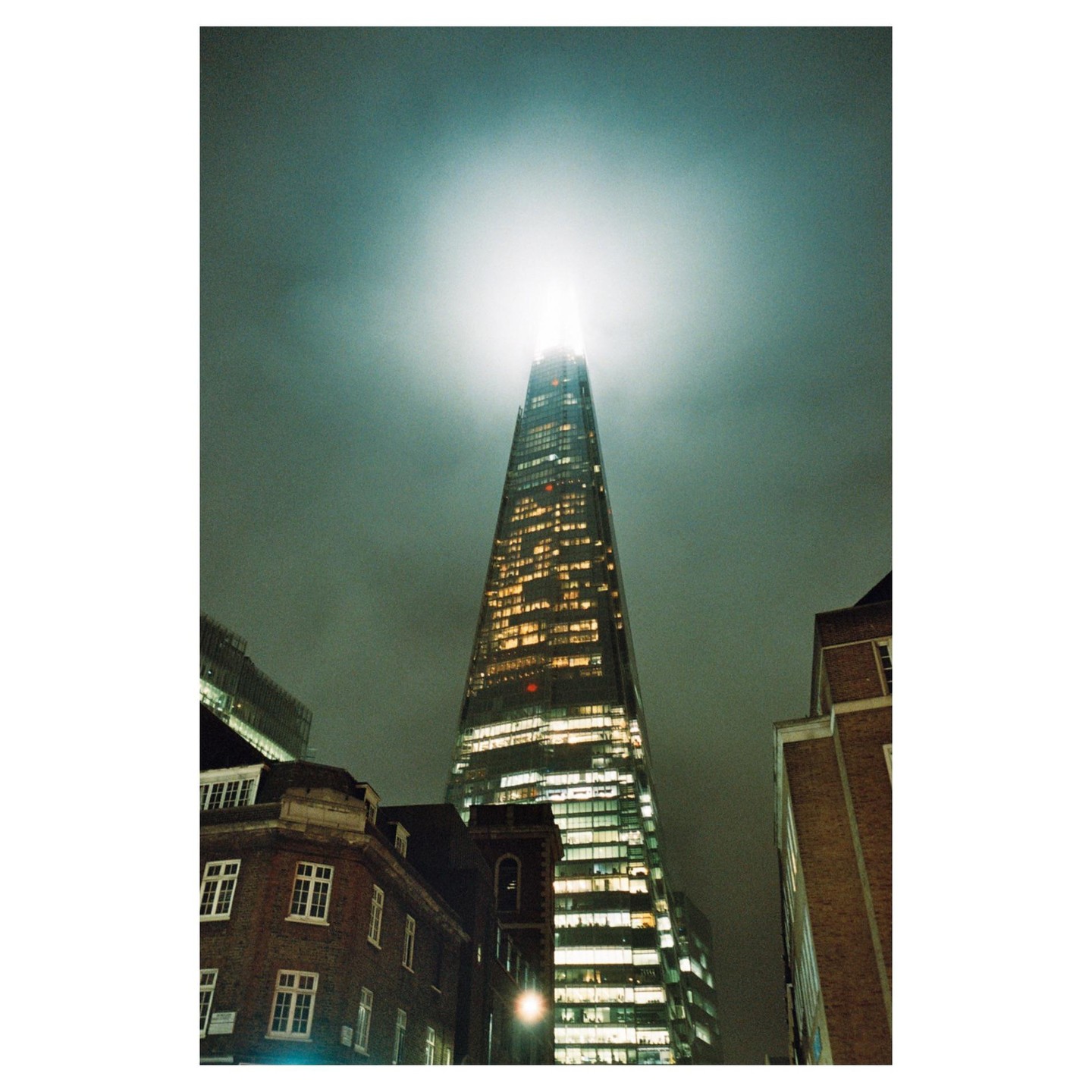 The Shard skyscraper rises into a cloudy night sky, surrounded by other buildings.