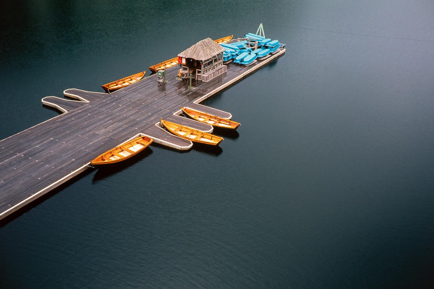 A wooden dock with a small hut and several boats extends into a calm lake.