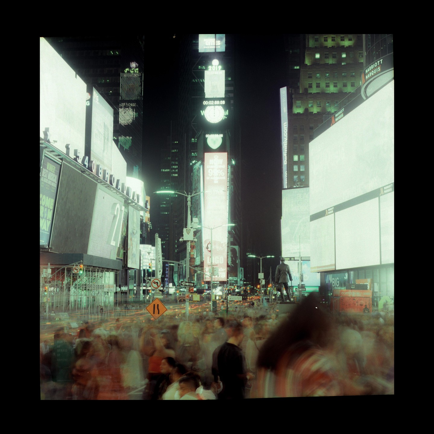 A long exposure captures the movement of people and traffic at night in Times Square, surrounded by bright billboards and buildings.