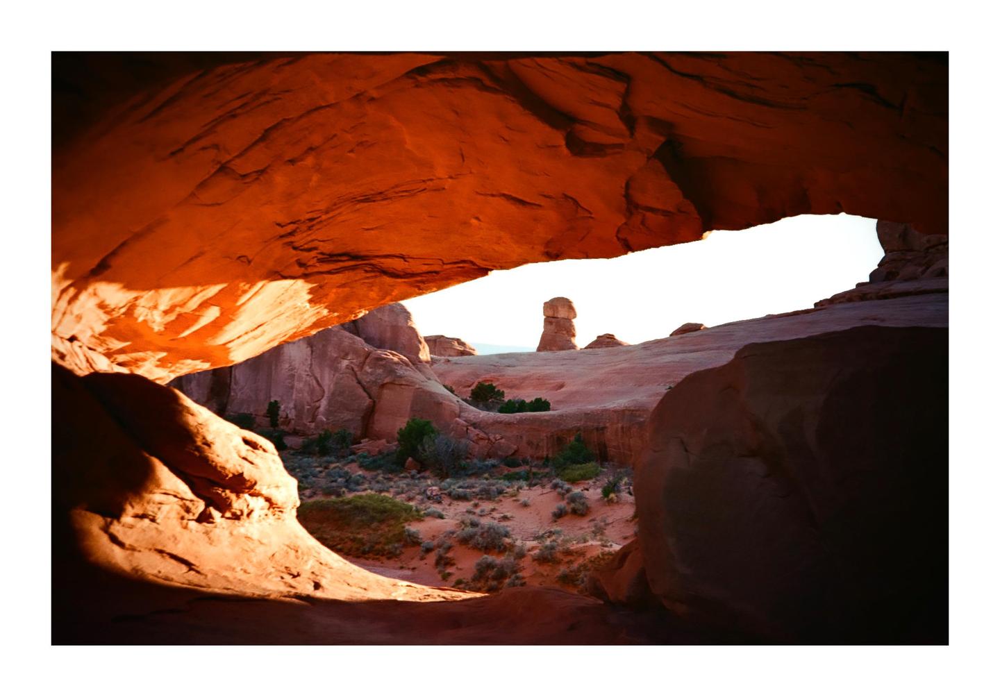 A natural arch frames a desert landscape with a rock formation in the distance.