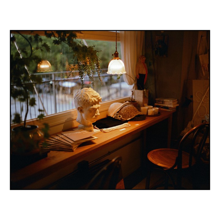 A white bust of a man sits on a wooden shelf next to a window, with two hanging lamps illuminating the scene.