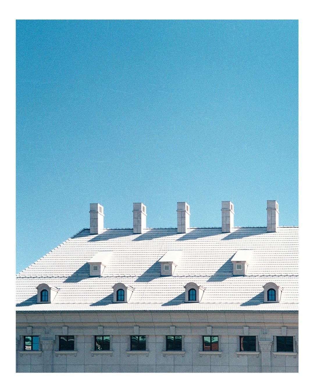 A white tiled roof with multiple chimneys and dormer windows sits below a clear blue sky.
