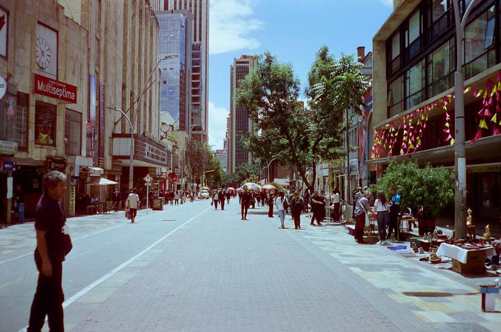 A man stands on a wide street with many people and tall buildings in the background.