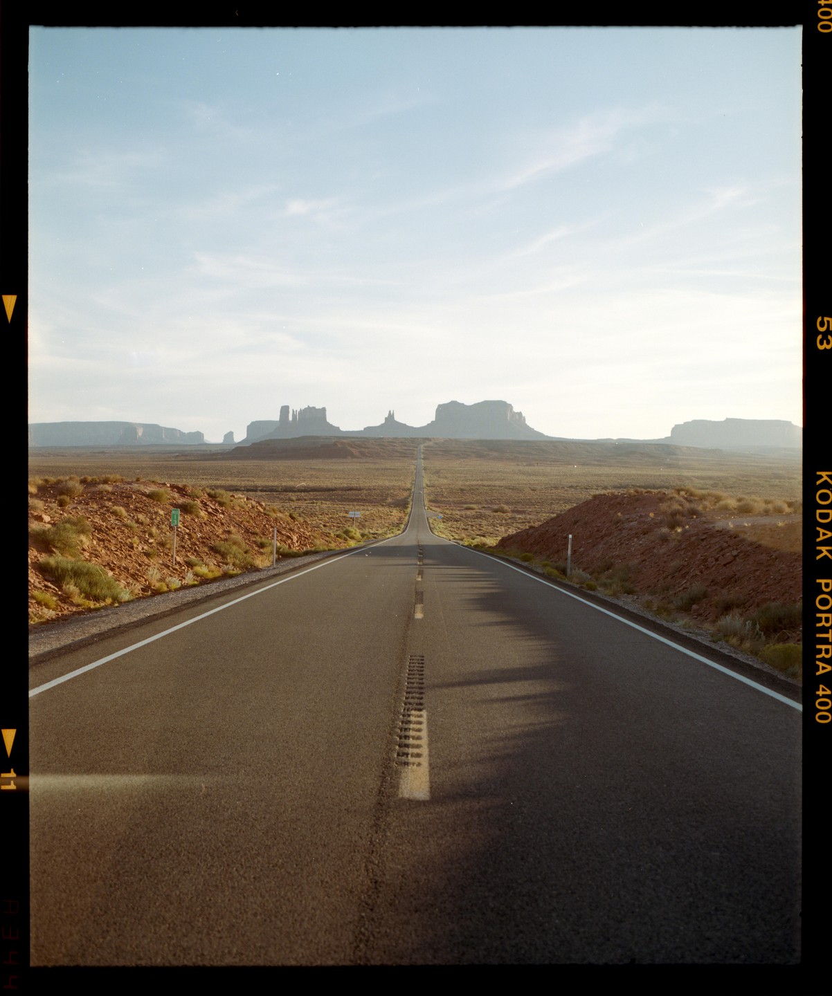 A long, straight road leads toward distant mesas under a bright sky.