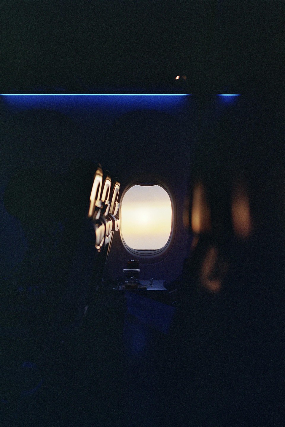 The interior of an airplane cabin is visible with a bright window showing the sky outside.