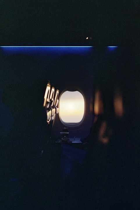 The interior of an airplane cabin is visible with a bright window showing the sky outside.