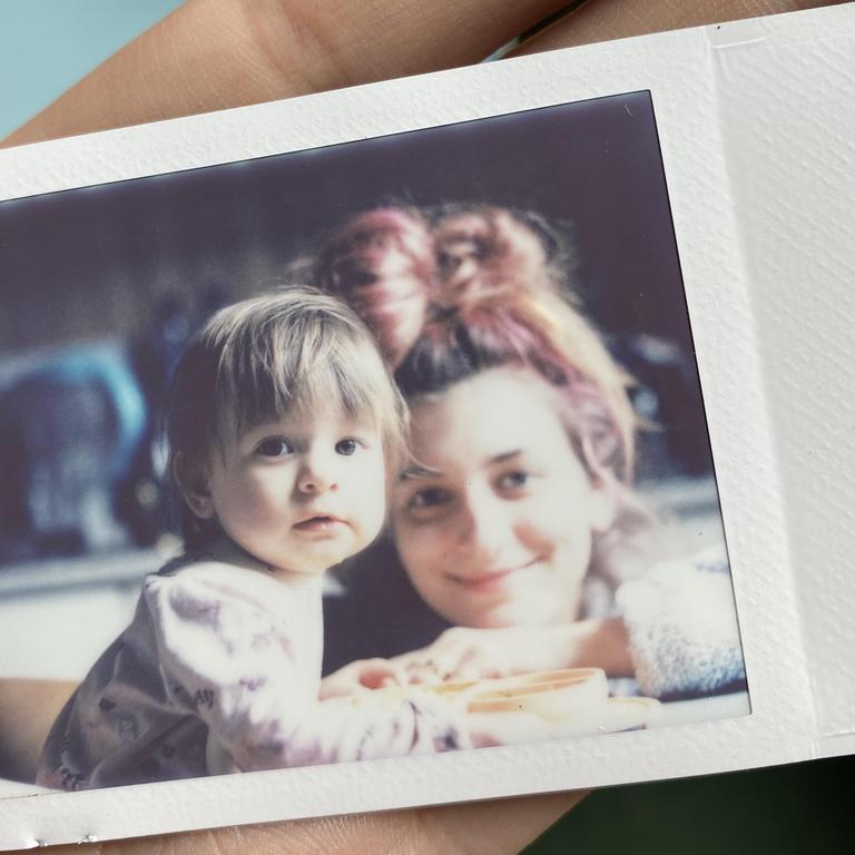 A woman with pink hair and a child are looking at the camera.