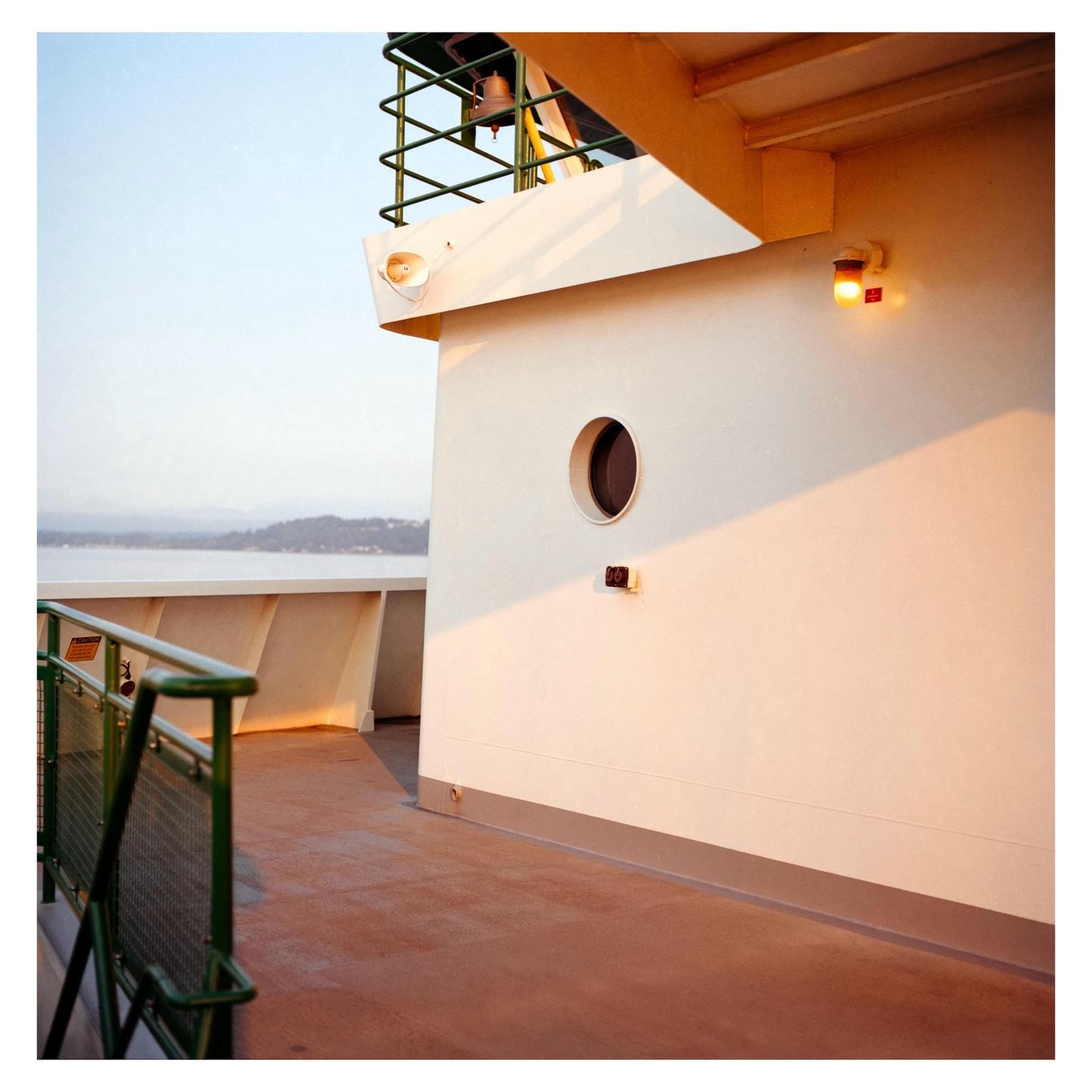 A ferry deck with a porthole and a light is illuminated by the sun.