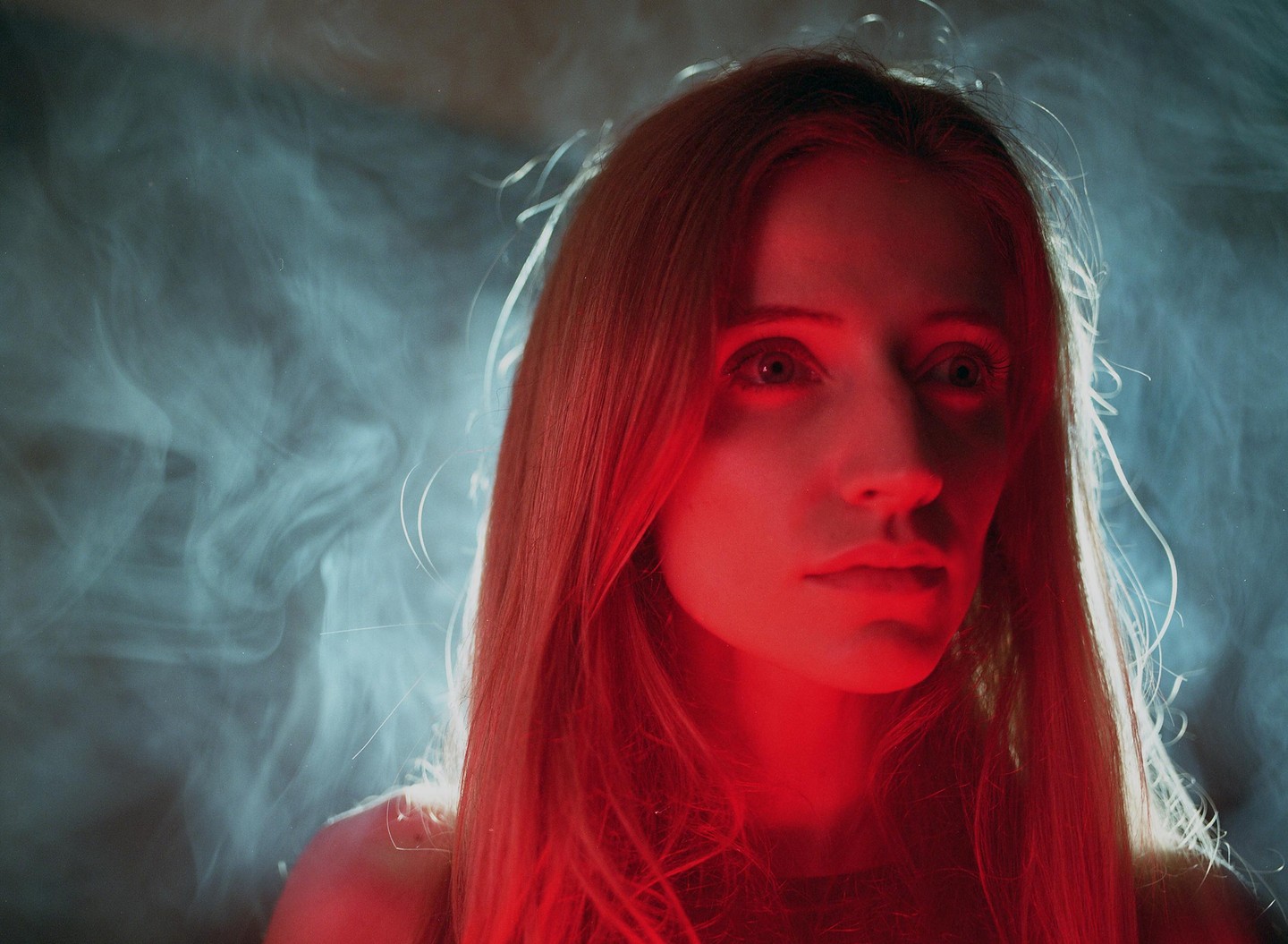 A woman with long hair is illuminated by red light against a hazy background.