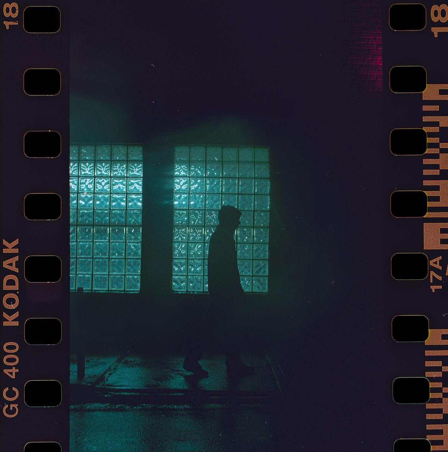 A man walks past two large windows made of glass blocks at night.