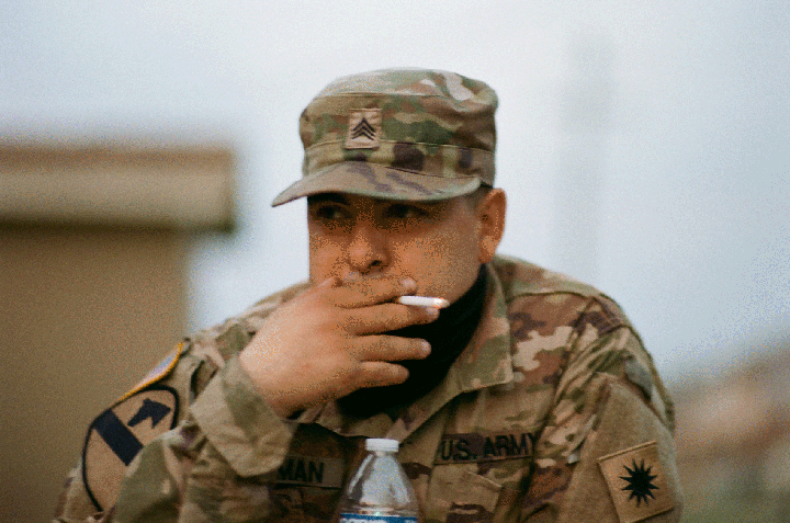 A man in a military uniform and cap smokes a cigarette.