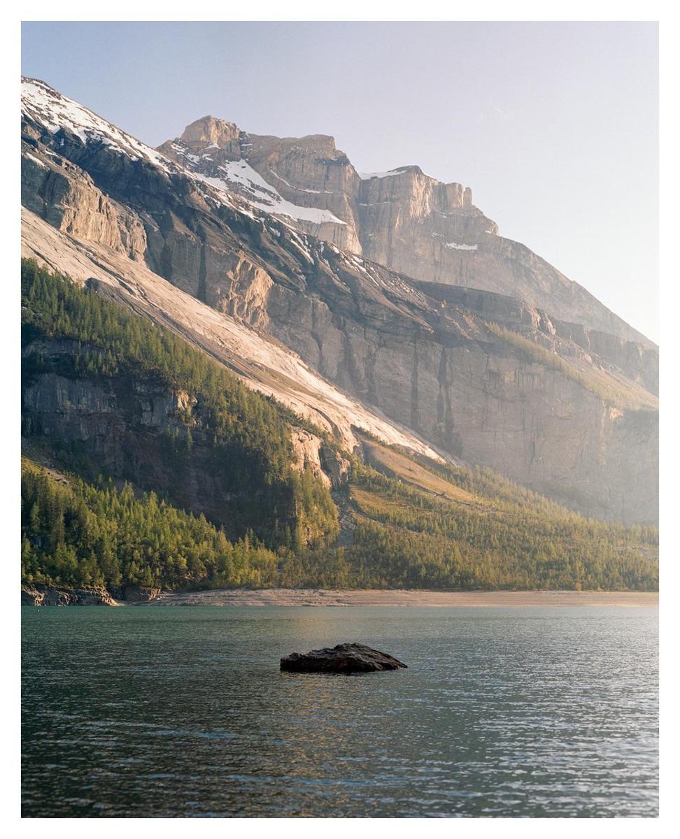 A large rock sits in a lake with a mountain and forest in the background during golden hour.