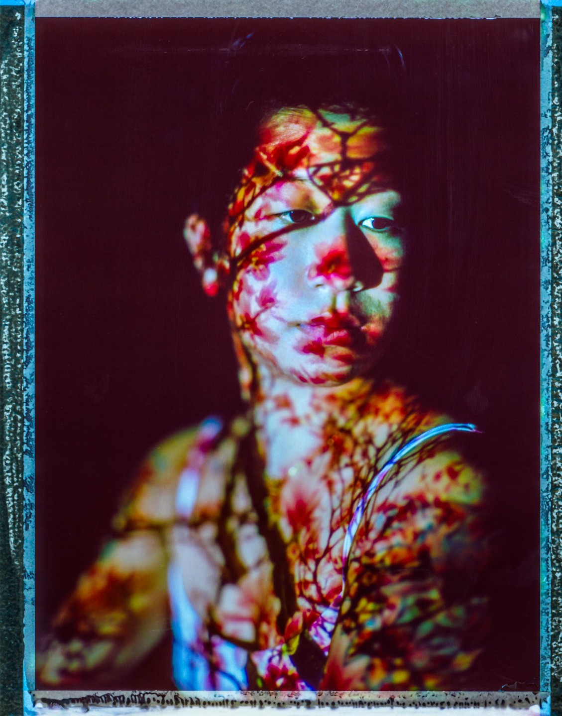 A woman's face and upper body are illuminated by a projection of colorful flowers and branches.