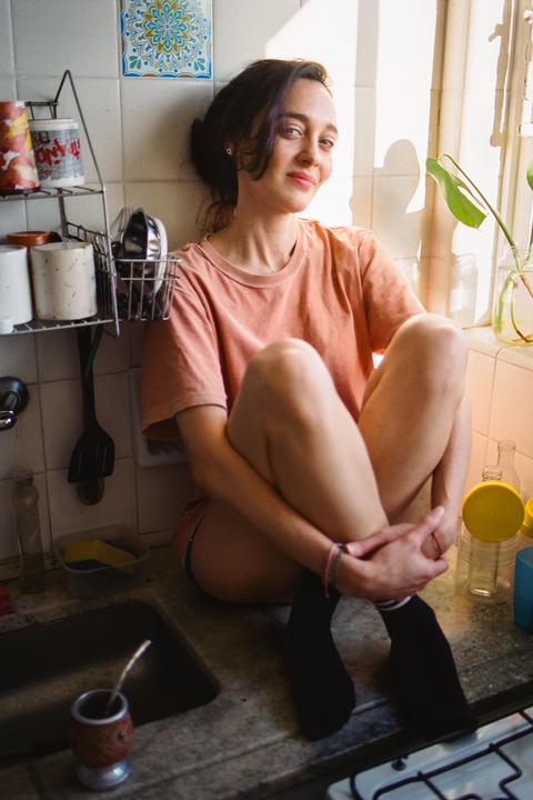 A woman sits on a kitchen counter with sunlight streaming in from a window.