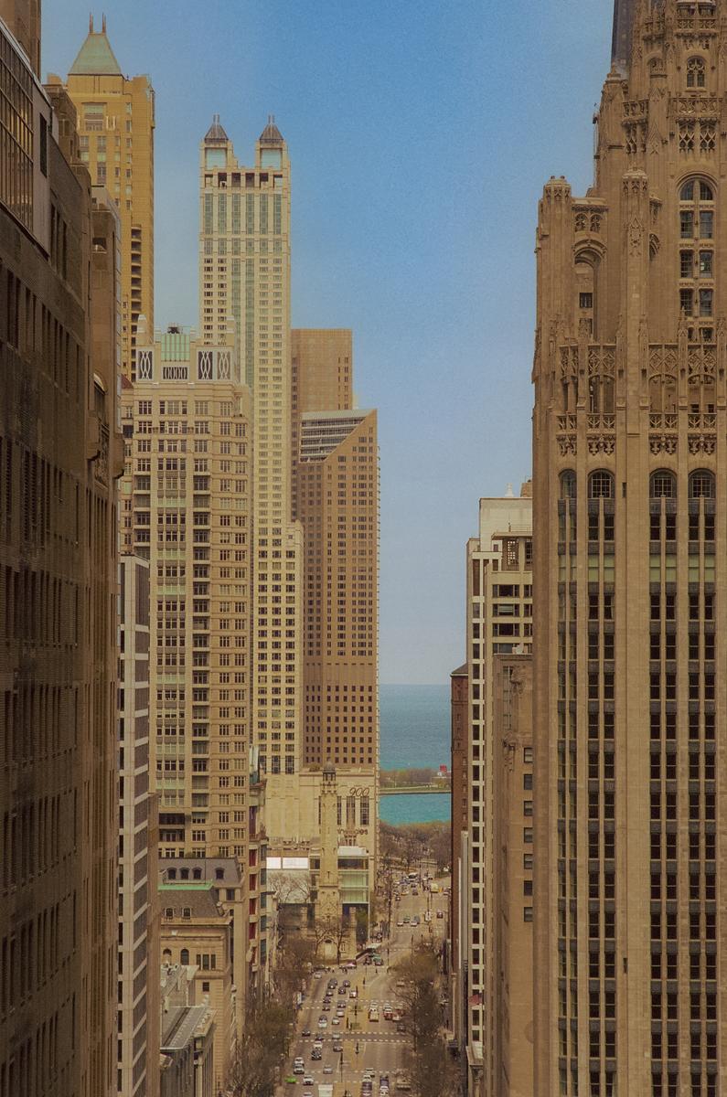 A street with cars and buildings on either side leads to a body of water in the distance.