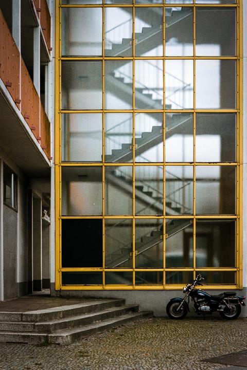 A motorcycle is parked in front of a building with a large window and a visible staircase.