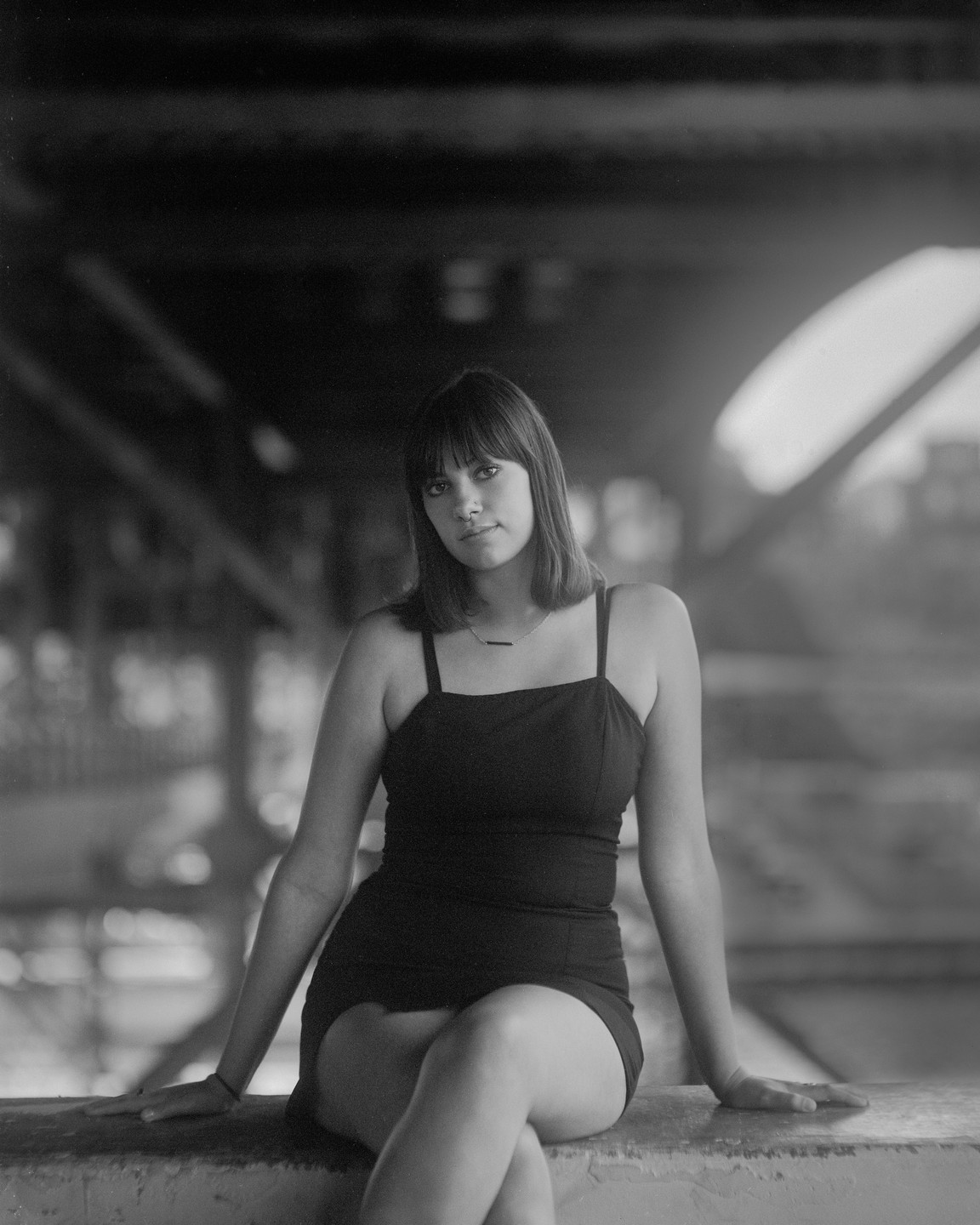 A woman in a dress sits on a ledge with her legs crossed.
