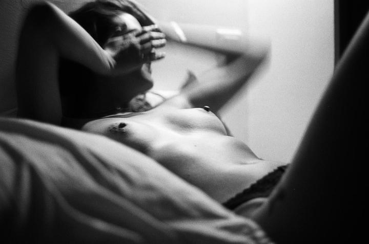 A woman lies on her back with her arms raised and hands covering her face.
