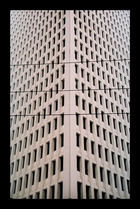 A tall building with many windows is seen from a low angle, with power lines crossing the frame.
