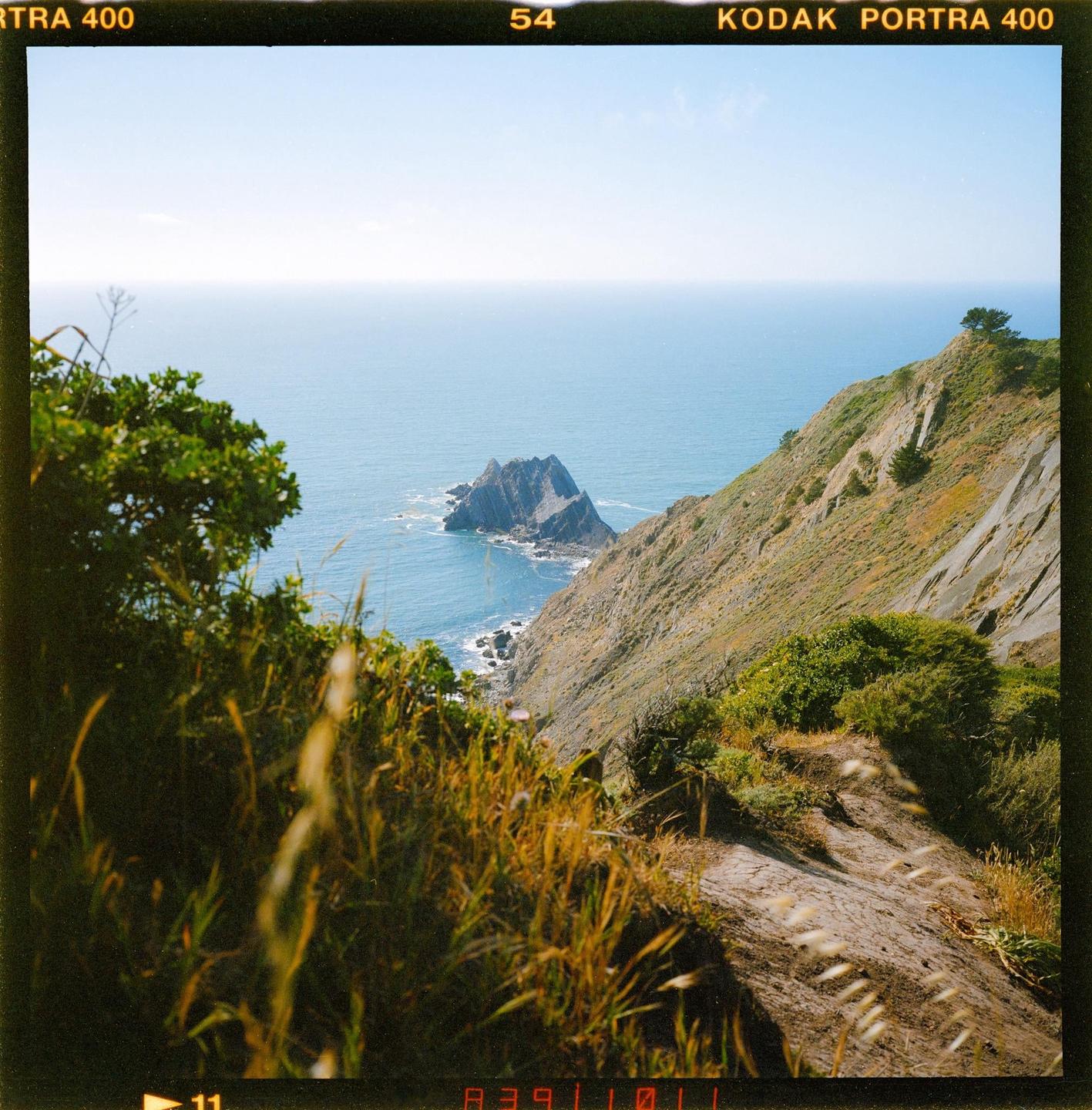 A rocky coastline with a steep cliff and a small island in the ocean.