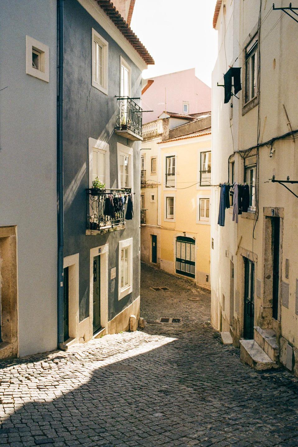 A narrow cobblestone street is lined with colorful buildings, some with laundry hanging from balconies and windows.