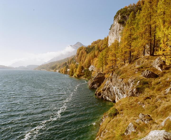 A body of water is next to a rocky, tree-covered mountain under a clear sky.