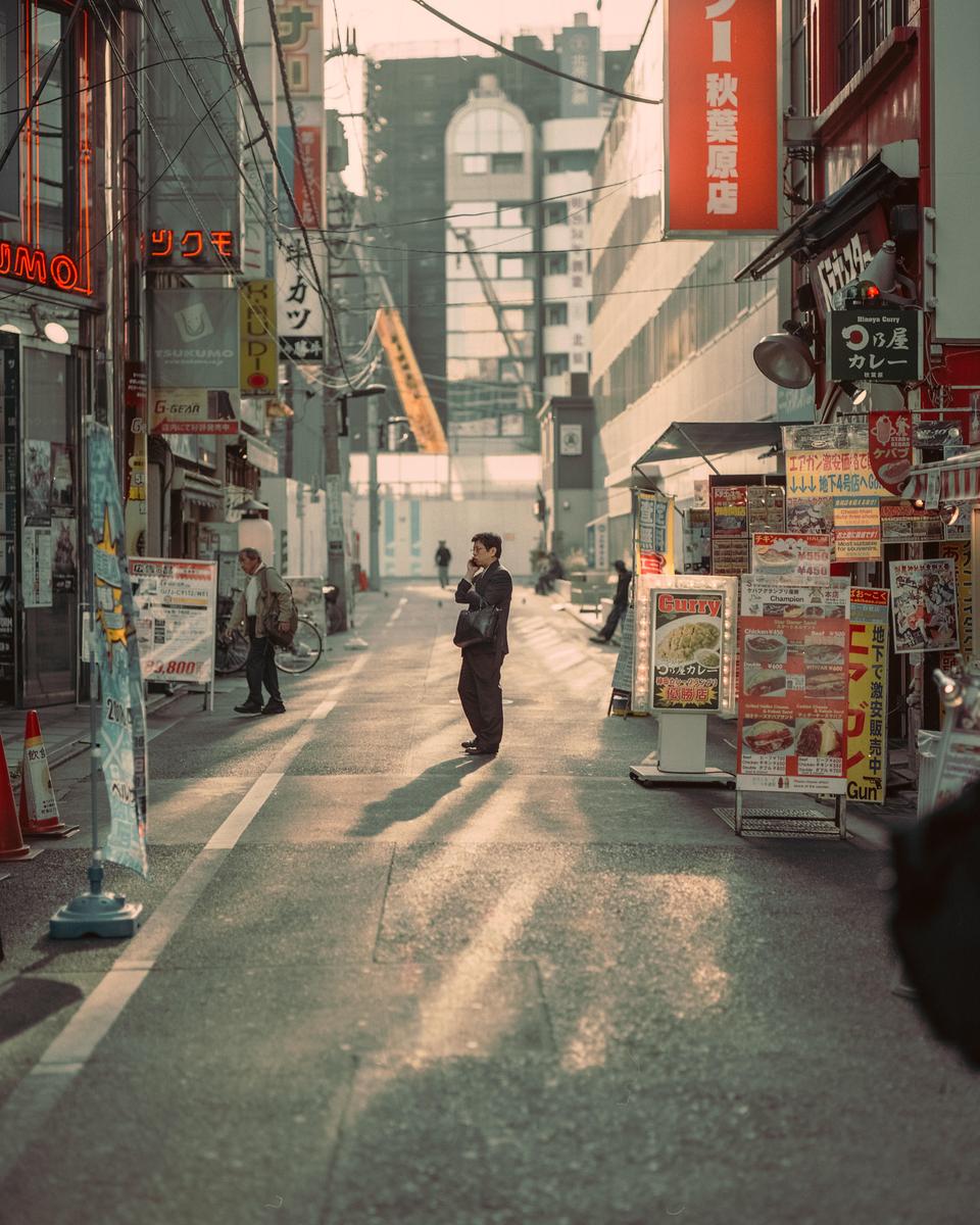 A man stands in the middle of a narrow street lined with buildings and signs in Tokyo.
