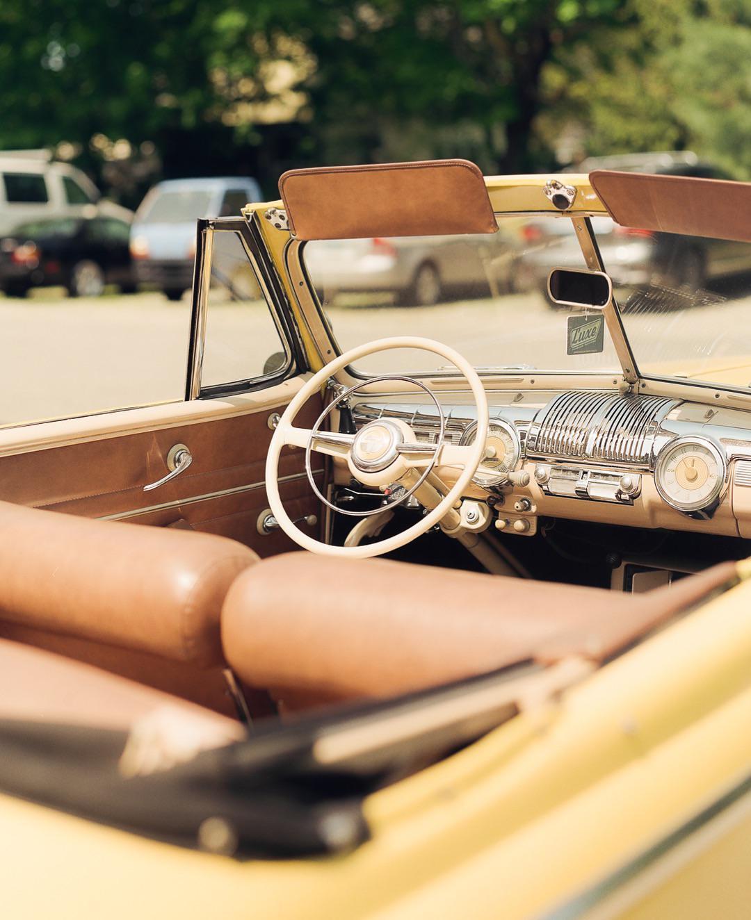 The interior of a vintage yellow convertible car with brown leather seats and a white steering wheel is visible.