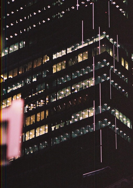 A tall building with many illuminated windows is seen at night, with vertical light strips on its facade.