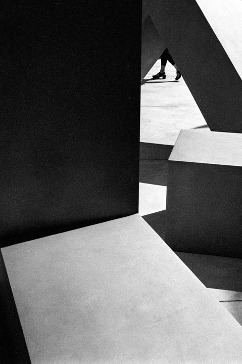 A person's legs and feet are visible through an opening between large geometric structures.