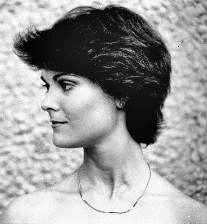 A woman with short hair and a necklace is shown in profile.