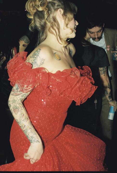 A woman in a red dress with tattoos on her arms and chest is dancing at a party.