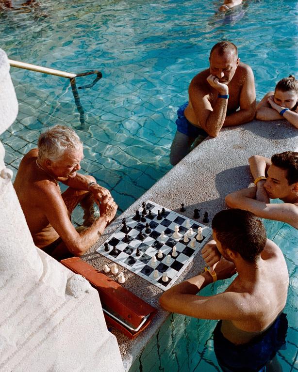 Four people are playing chess in a swimming pool on a sunny day.