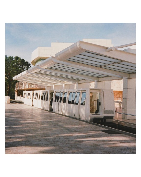 A white monorail train is parked at a station platform with a modern building in the background.