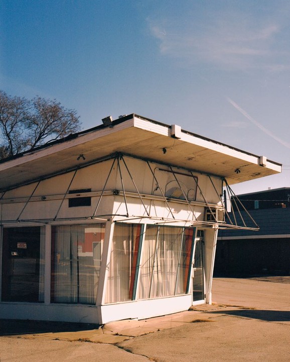 A small, white, mid-century modern building with large windows and a flat roof stands under a clear blue sky.