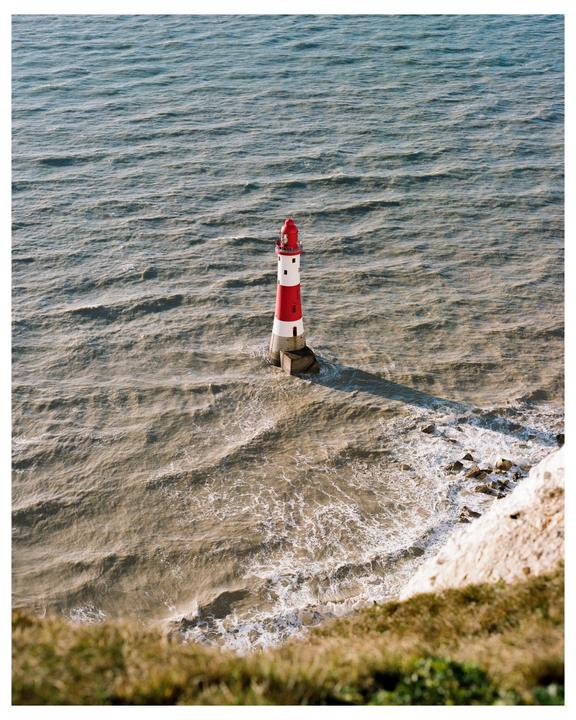 A red and white lighthouse stands in the ocean with waves crashing around its base.
