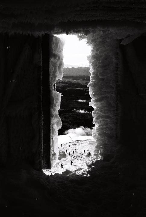 A group of skiers is visible on a snowy mountain slope through a snow-covered opening.