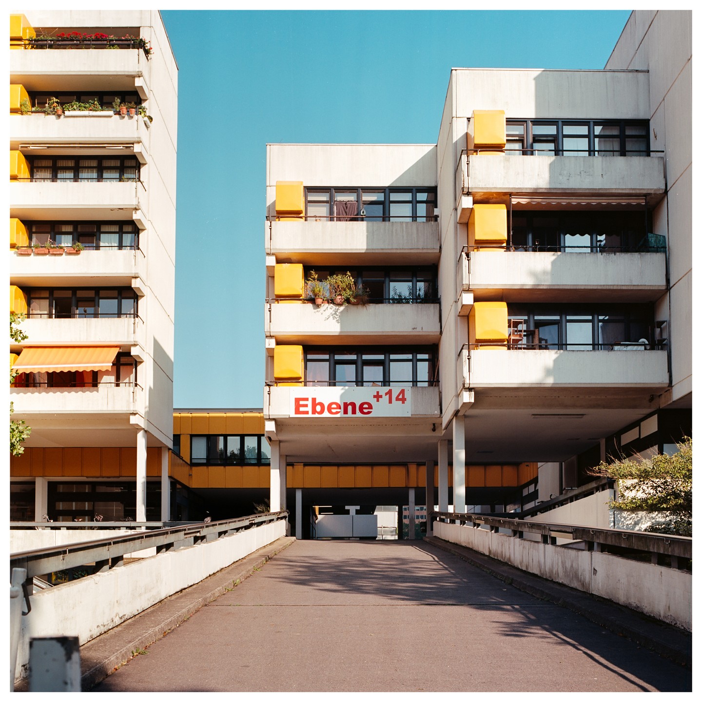 A concrete ramp leads to a parking garage under a large apartment building with yellow accents.