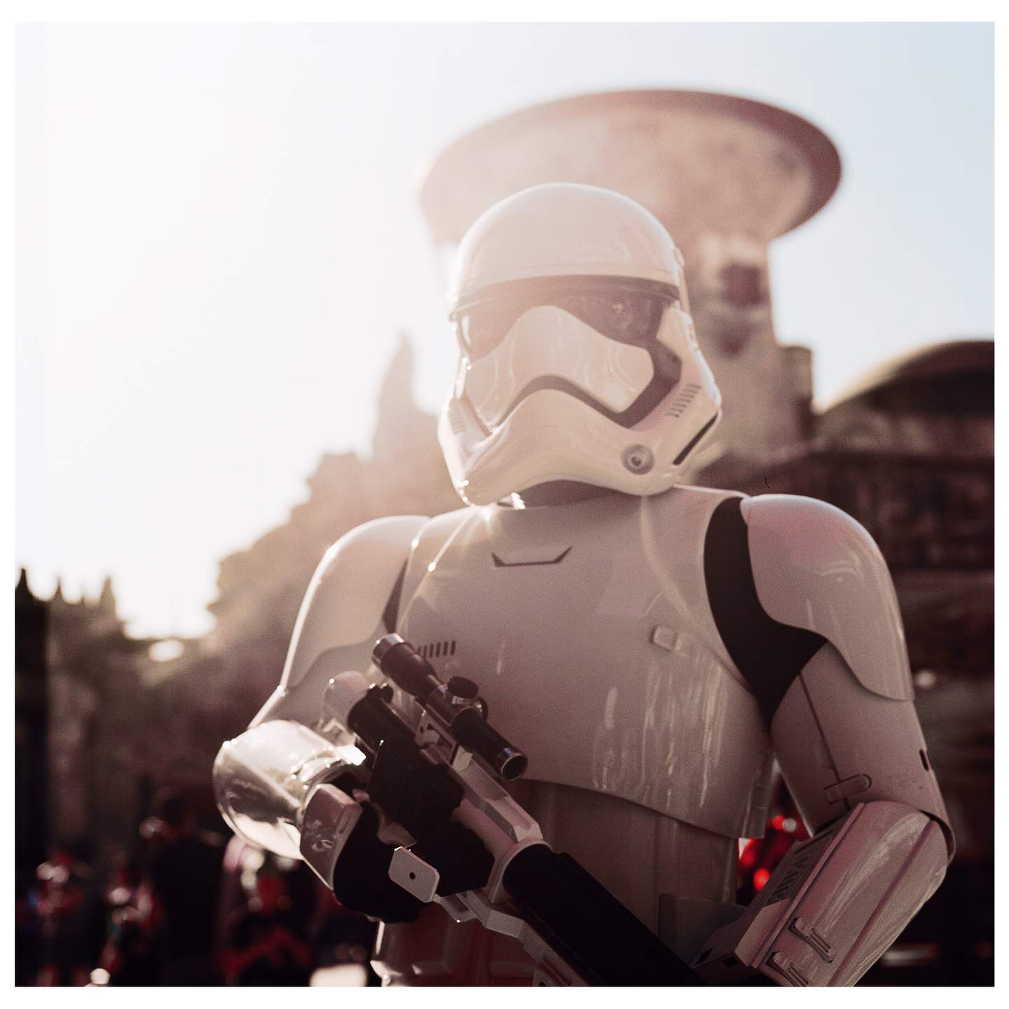 A stormtrooper in white armor holds a weapon while standing in a sunlit outdoor setting.