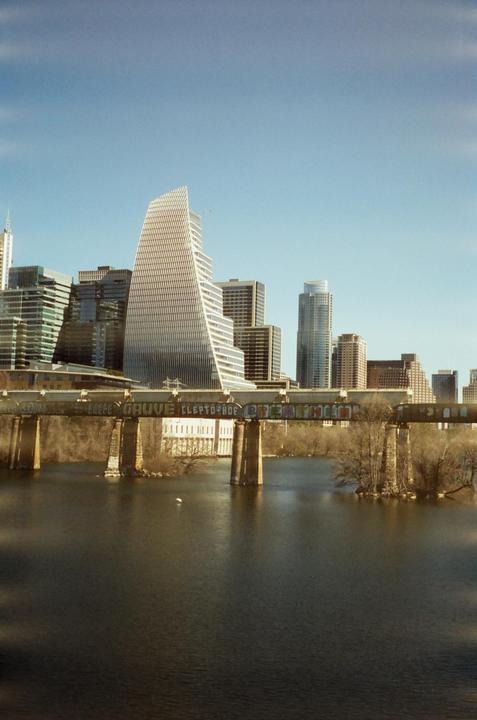 A cityscape with a river and a bridge covered in graffiti in the foreground.