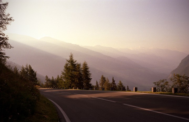 A winding road curves through a mountainous landscape with trees and hazy light.