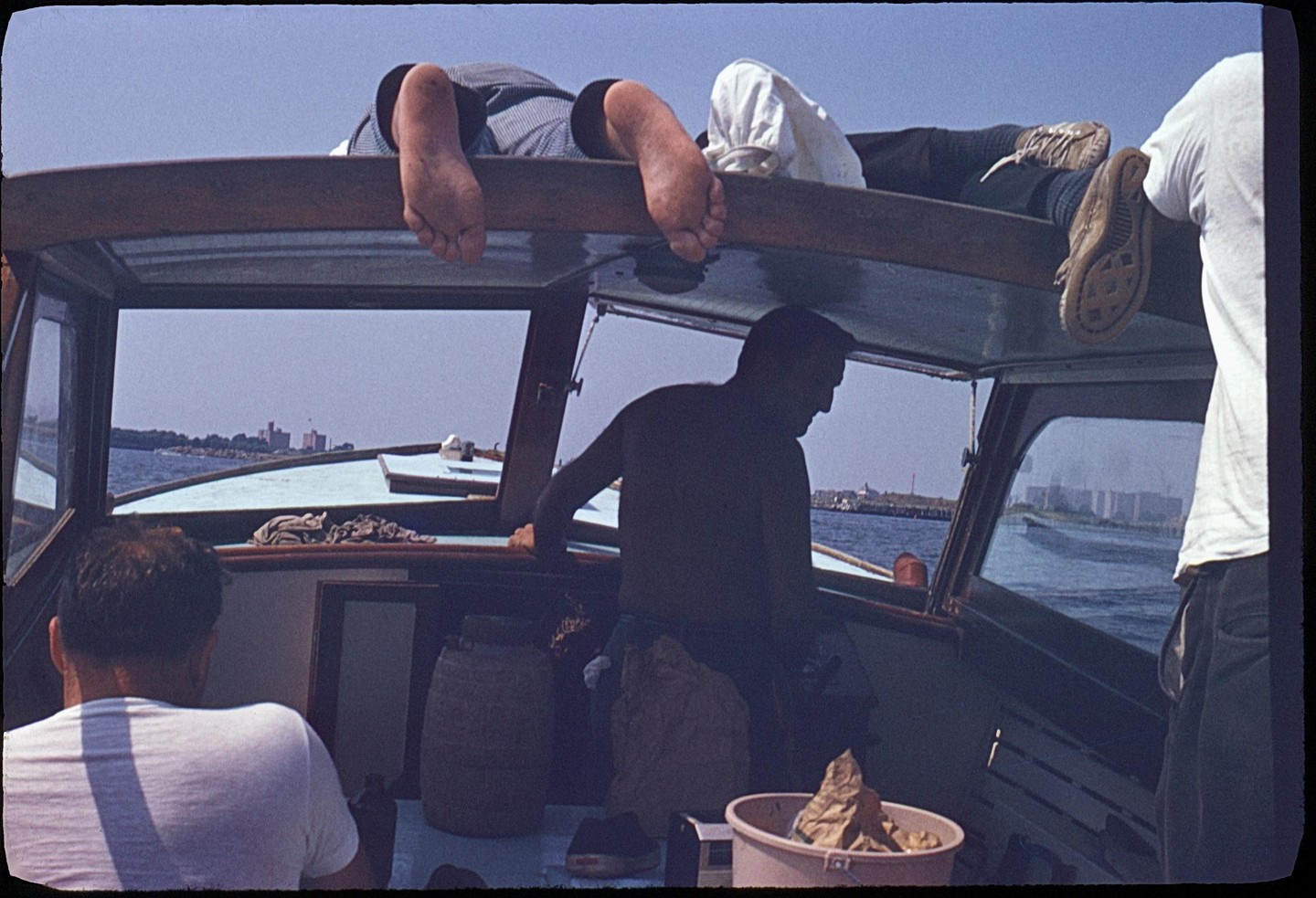 Three men are on a boat, with two men visible from the waist down relaxing on the roof of the boat, and one man in the cabin.