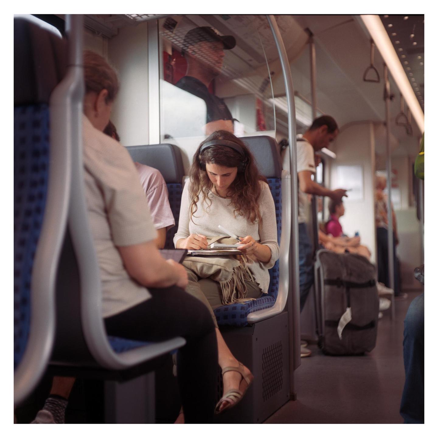 A woman wearing headphones is drawing in a notebook while riding a train.