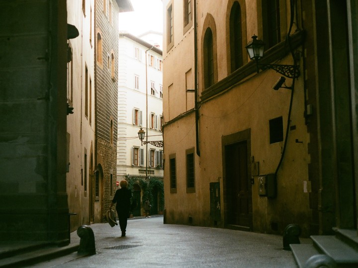 A woman walks down a narrow, old street lined with tall buildings in Florence.